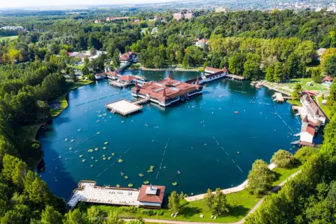 Malownicze jezioro Balaton z termalnymi basenami i otaczającym je lasem. Ludzie pływają i relaksują się w wodzie.