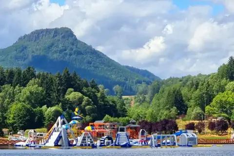 Kolorowy park wodny na wodzie przy górskim krajobrazie. **Radków zalew** zaprasza do zabawy na dmuchanych zjeżdżalniach i torach przeszkód.
