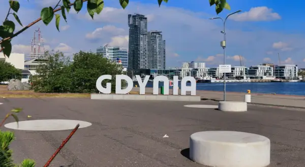Napis "GDYNIA" na tle nowoczesnych budynków i portu.
