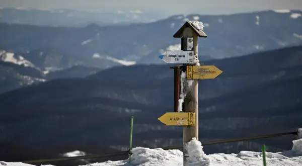 Zimowy szlak w górach. Drewniany słup z drogowskazami, na którym widnieje napis "Ustrzyki Górne 2 h" i "WIATA-45". Mała rawka śniegu ozdabia szczyt drogowskazu.