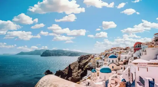 Santorini, Grecja. Białe domki z niebieskimi kopułami na klifie nad morzem. Idealne miejsce na wakacje, zastanawiasz się, ile się leci do Grecji?