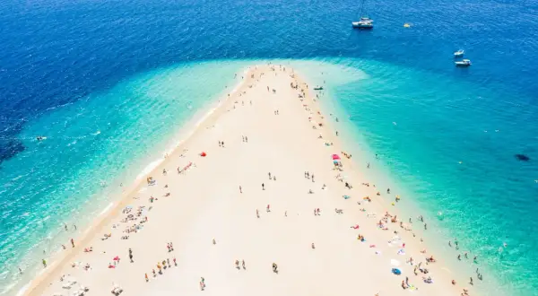 Złoty róg Chorwacja, plaża z turkusową wodą i ludźmi odpoczywającymi na piasku. W oddali widać łodzie.