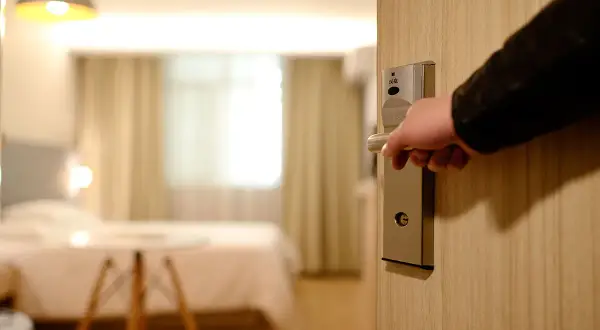 Otwieranie drzwi hotelowego pokoju, w którym panuje **overbooking**. Wnętrze jest puste, łóżko pościelone, a zasłony zasunięte.
