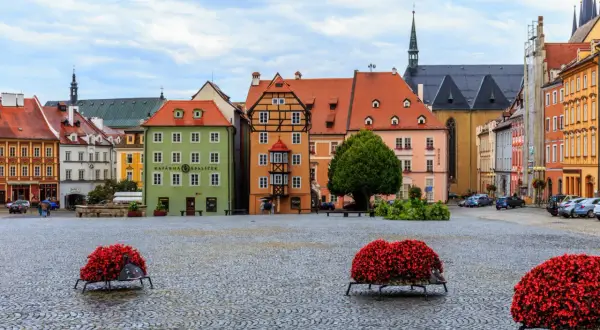 Kolorowy rynek w Chebie z kamienną nawierzchnią i ozdobnymi donicami z czerwonymi kwiatami.