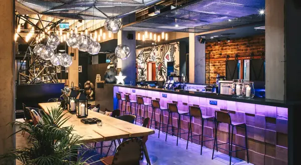 Nowoczesny bar w Moxy Hotels Pyrzowice z neonowym oświetleniem, drewnianym blatem i artystycznymi muralami.