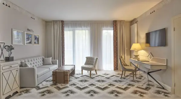 Elegancki pokój hotelowy z sofą, fotelem i biurkiem. Wnętrze w stylu 4-gwiazdkowym, z dywanem o geometrycznym wzorze.