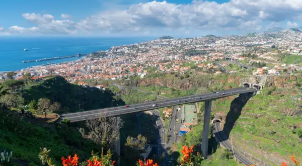 Widok na Funchal, Maderę, z autostradą przecinającą dolinę i wpadającą do tuneli. W oddali widać ocean i port.