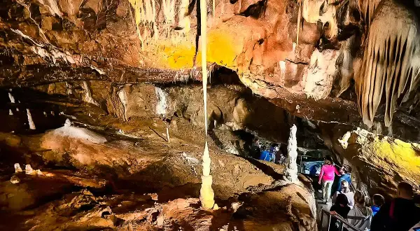 Wnętrze jaskini Macochy, z naciekami i stalagmitami. Grupa turystów schodzi po schodach, podziwiając podziemne piękno.