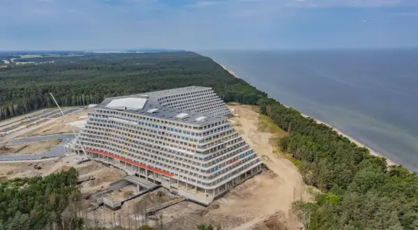 Ogromny hotel w kształcie tarasów w budowie, nad morzem, otoczony lasem.
