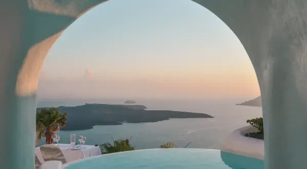 Romantyczne Santorini wakacje: basen z widokiem na kalderę, stół nakryty do kolacji przy zachodzie słońca. Idealne miejsce na niezapomniany pobyt.