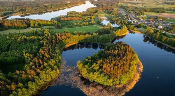 Widok z lotu ptaka na jezioro otoczone lasem i małą wioskę na Mazurach.