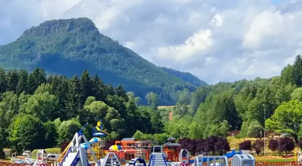Kolorowy park wodny na wodzie przy górskim krajobrazie. **Radków zalew** zaprasza do zabawy na dmuchanych zjeżdżalniach i torach przeszkód.