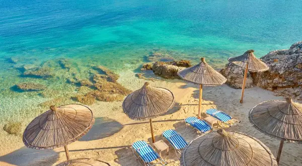 Albania - wczasy samolotem all inclusive. Słoneczna plaża z leżakami i parasolami, turkusowe morze. Idealne miejsce na relaks.