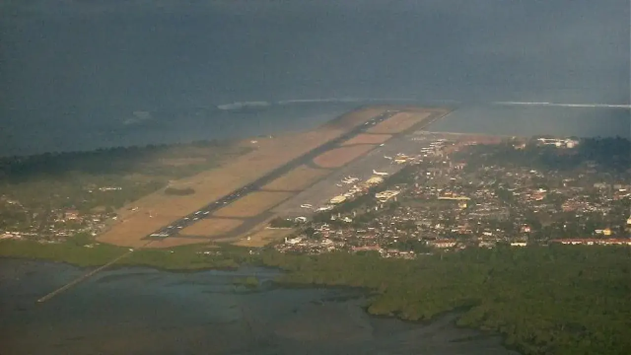 Widok z lotu ptaka na lotnisko na Bali, z pasem startowym biegnącym wzdłuż wybrzeża i miastem w tle.