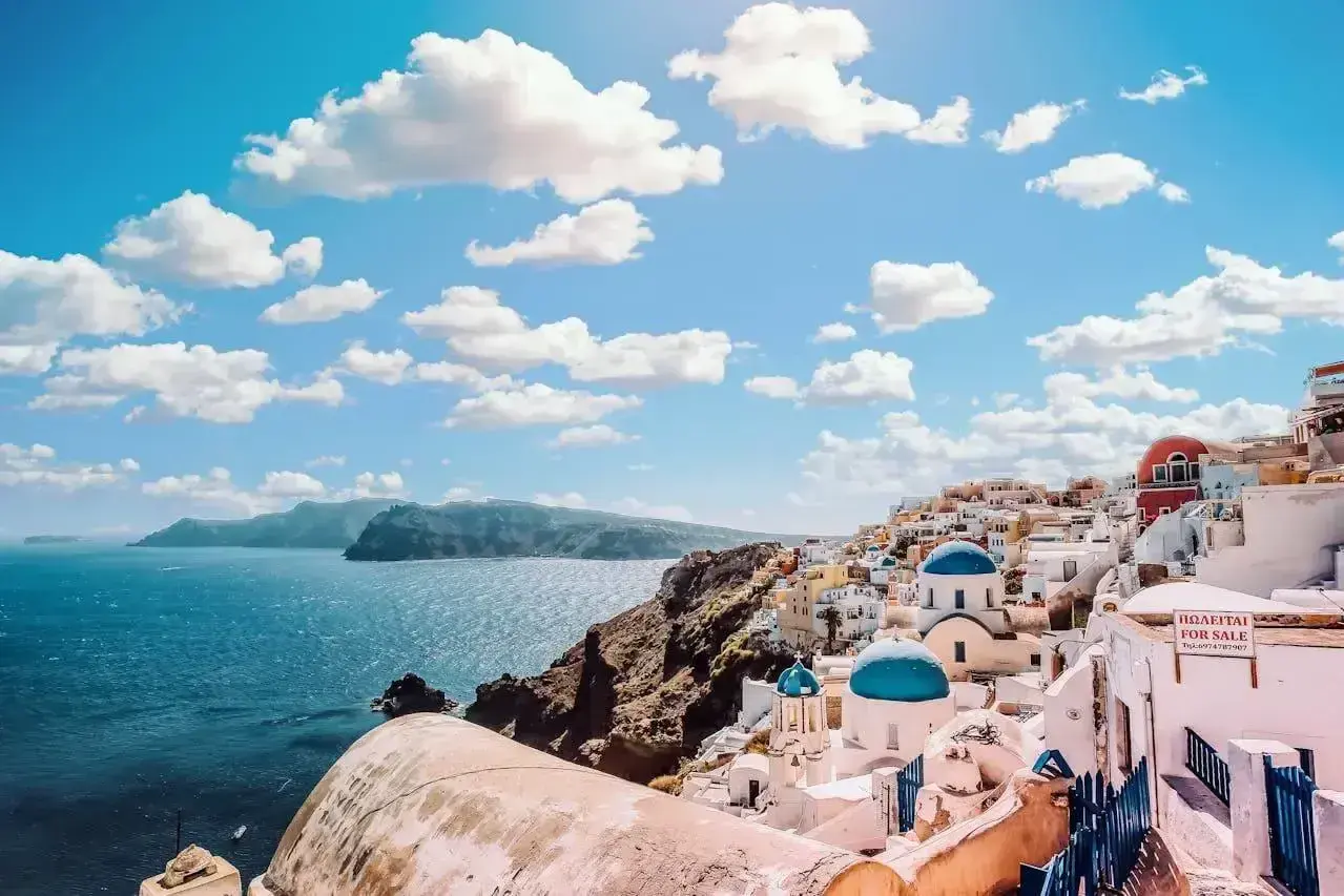 Santorini, Grecja. Białe domki z niebieskimi kopułami na klifie nad morzem. Idealne miejsce na wakacje, zastanawiasz się, ile się leci do Grecji?