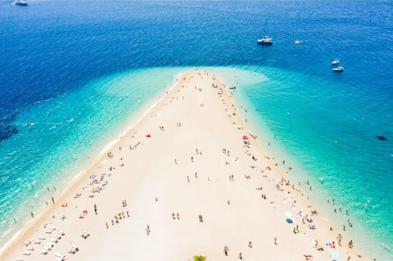 Złoty róg Chorwacja, plaża z turkusową wodą i ludźmi odpoczywającymi na piasku. W oddali widać łodzie.