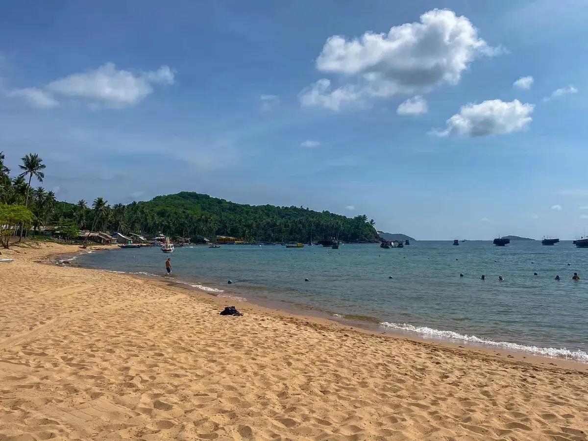 Piękna plaża i turkusowe morze, idealne na wietnam wakacje. W oddali widać łodzie i zieloną wyspę.