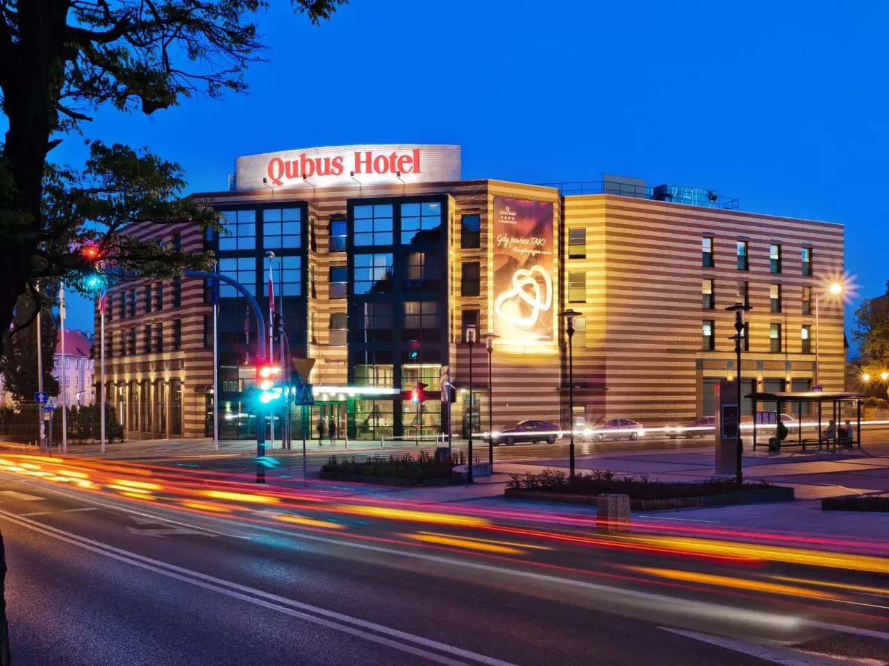 Hotel Qubus Gorzów nocą, z widocznymi światłami samochodów na ulicy i neonem hotelu.