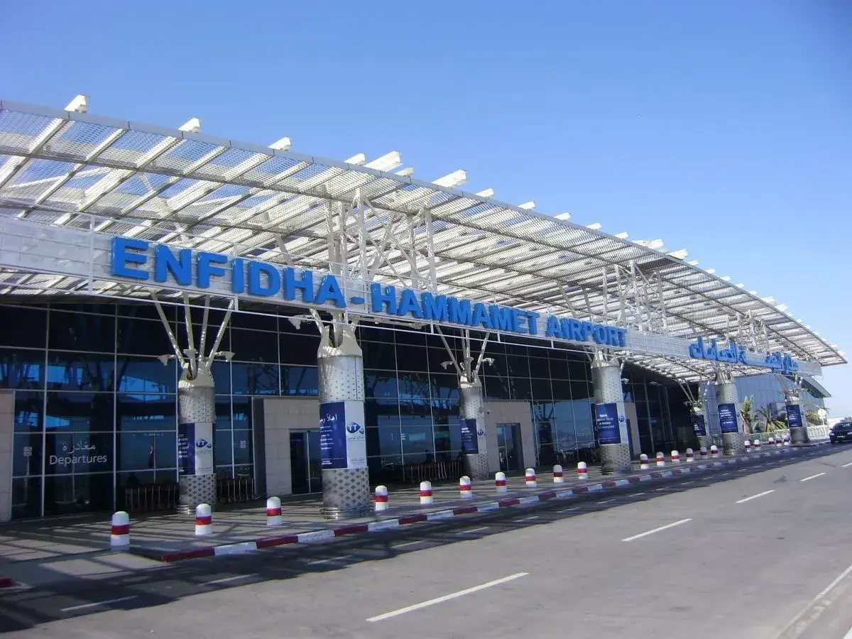 Nowoczesny budynek lotniska Enfidha-Hammamet w Tunezji, z niebieskimi literami nazwy i przeszkloną fasadą.
