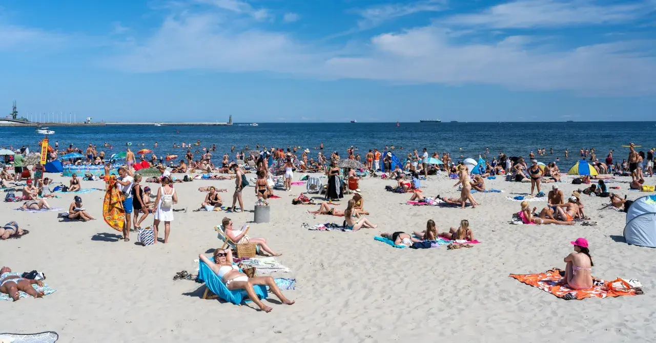 Tłumy ludzi na plaży, opalanie i kąpiel w morzu. Zastanawiasz się, ile kosztuje nocleg nad morzem w sezonie?