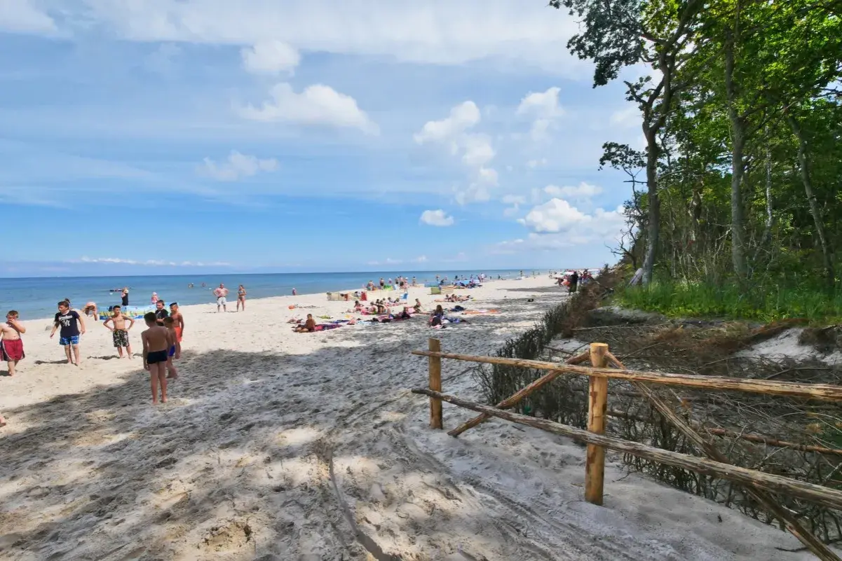 Słoneczny dzień na plaży w Karwieńskich Błotach. Ludzie odpoczywają na piasku, a morze spokojnie faluje.