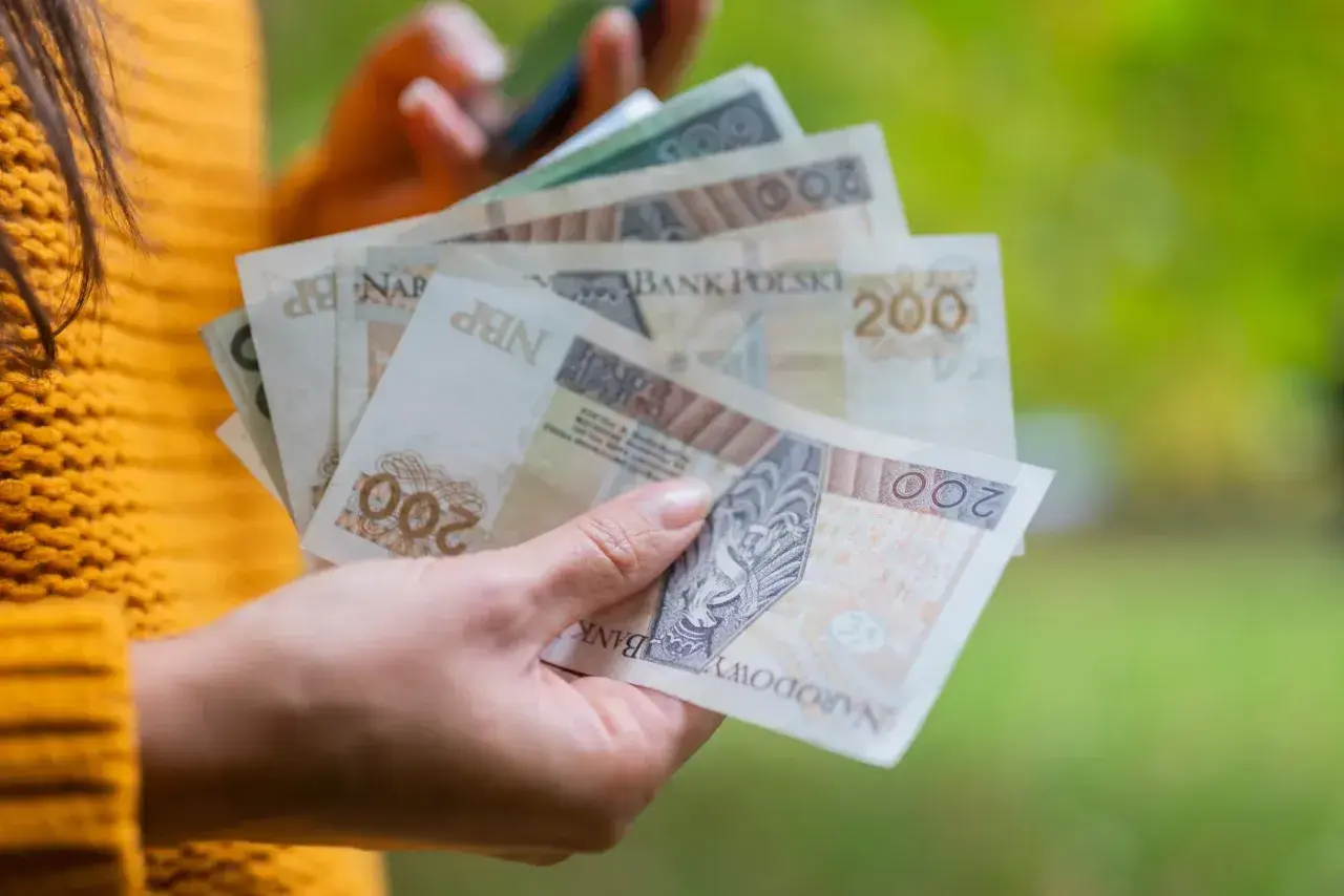 Dłoń trzyma polskie banknoty 200 zł. Zastanawiasz się, ile to netto po przekroczeniu drugiego progu podatkowego?