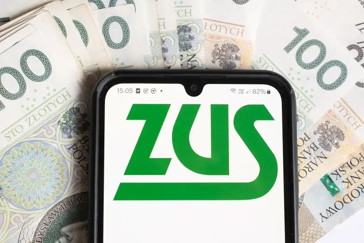 Telefon z logo ZUS na tle banknotów 100 zł. Czas na opłacenie składek ZUS.