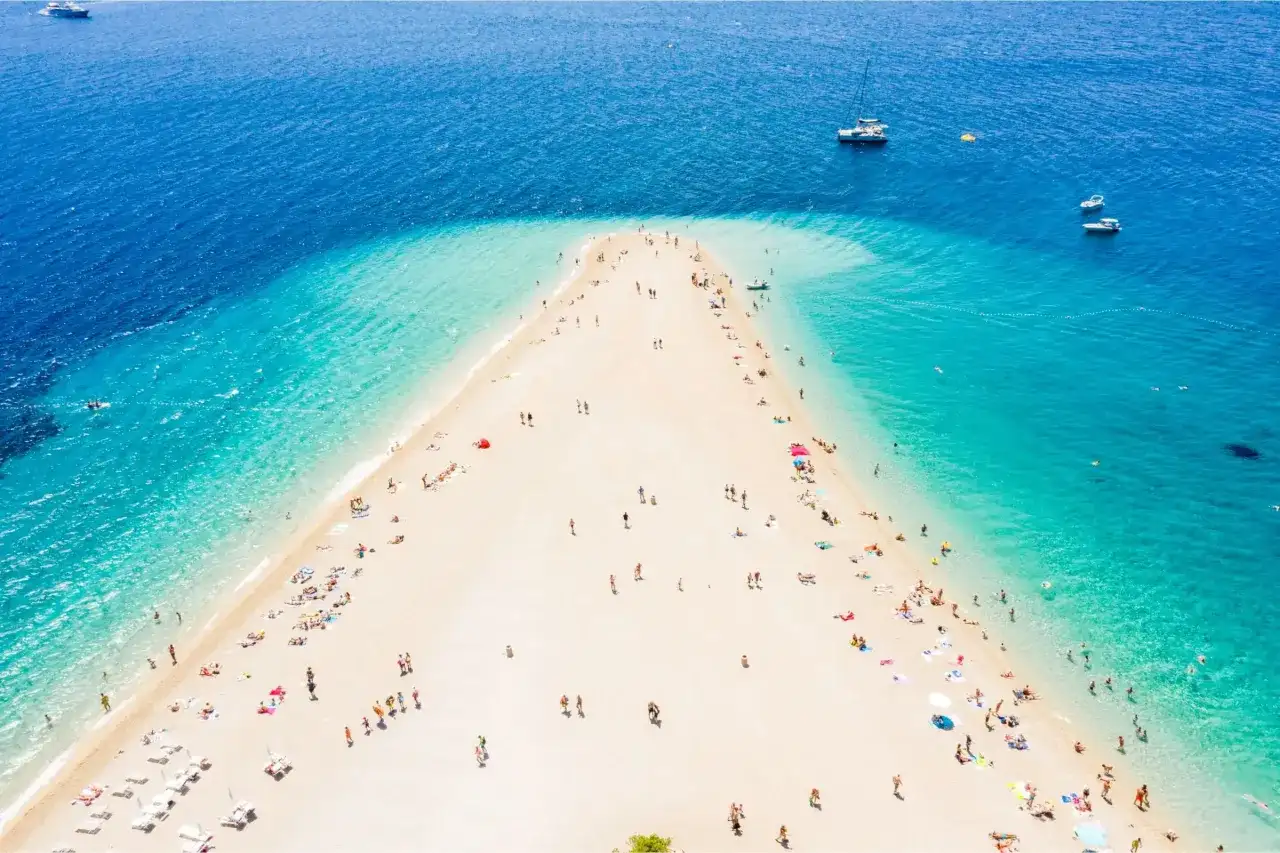 Złoty róg Chorwacja, plaża z turkusową wodą i ludźmi odpoczywającymi na piasku. W oddali widać łodzie.