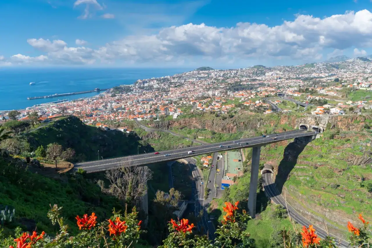 Widok na Funchal, Maderę, z autostradą przecinającą dolinę i wpadającą do tuneli. W oddali widać ocean i port.
