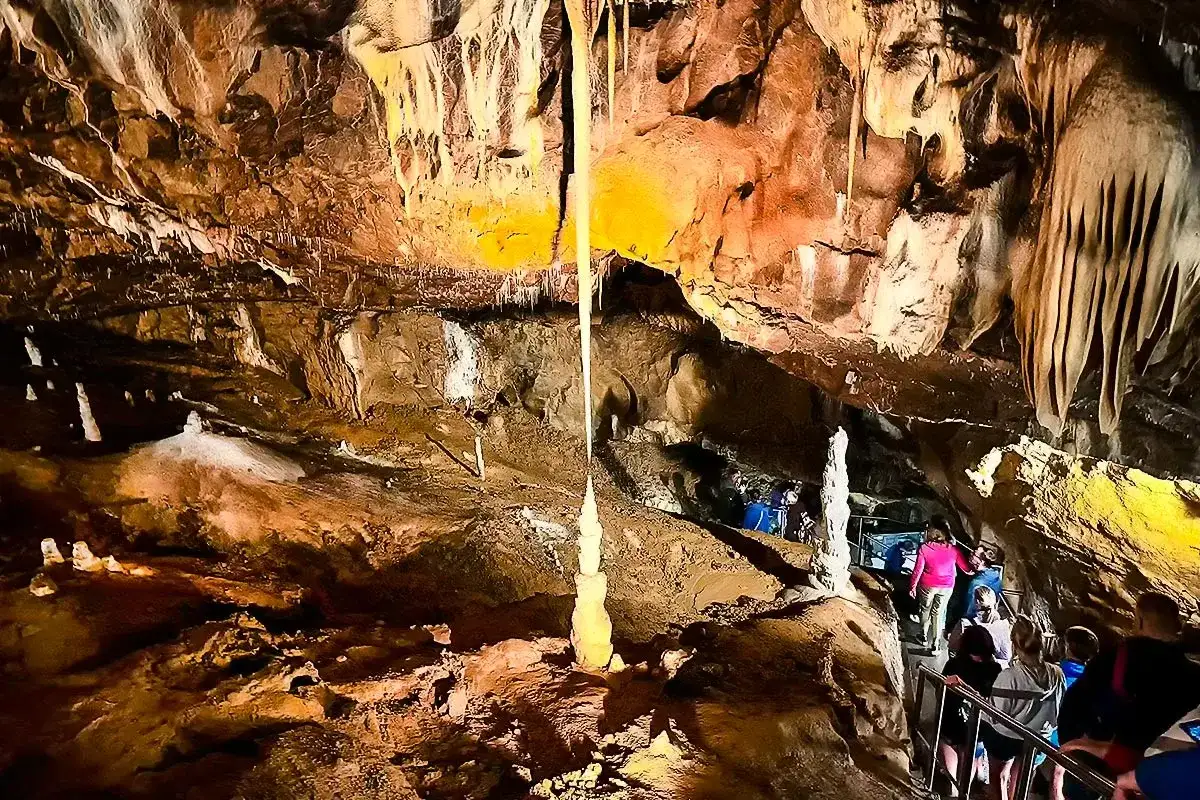 Wnętrze jaskini Macochy, z naciekami i stalagmitami. Grupa turystów schodzi po schodach, podziwiając podziemne piękno.