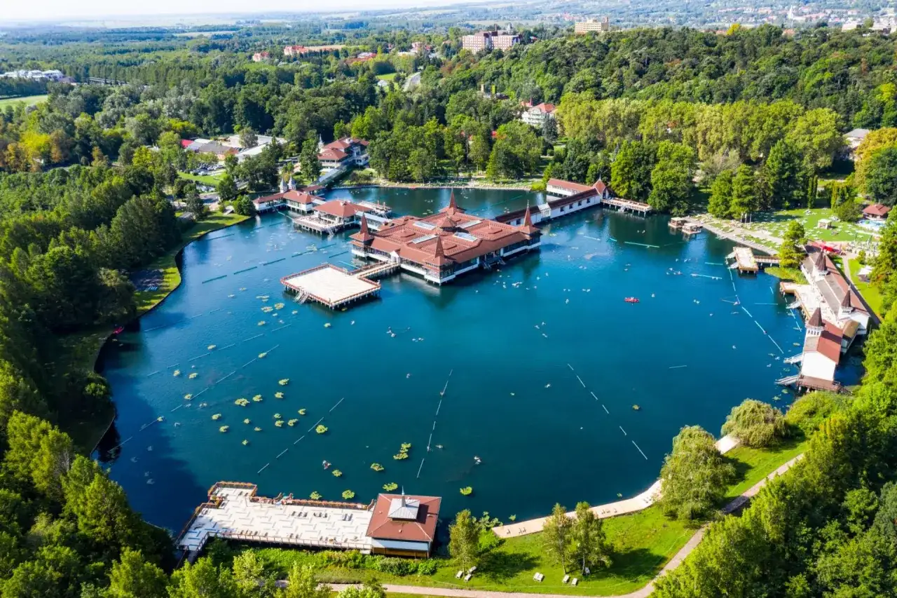 Malownicze jezioro Balaton z termalnymi basenami i otaczającym je lasem. Ludzie pływają i relaksują się w wodzie.