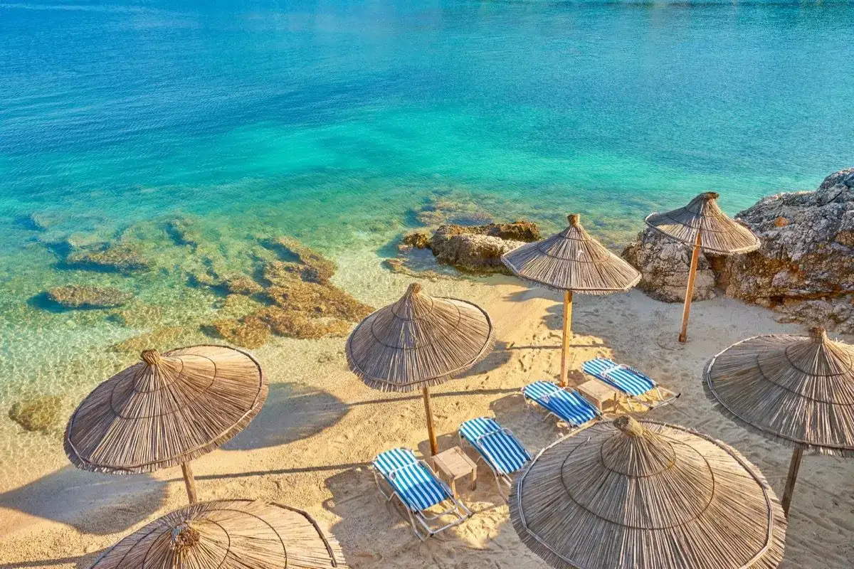Albania - wczasy samolotem all inclusive. Słoneczna plaża z leżakami i parasolami, turkusowe morze. Idealne miejsce na relaks.