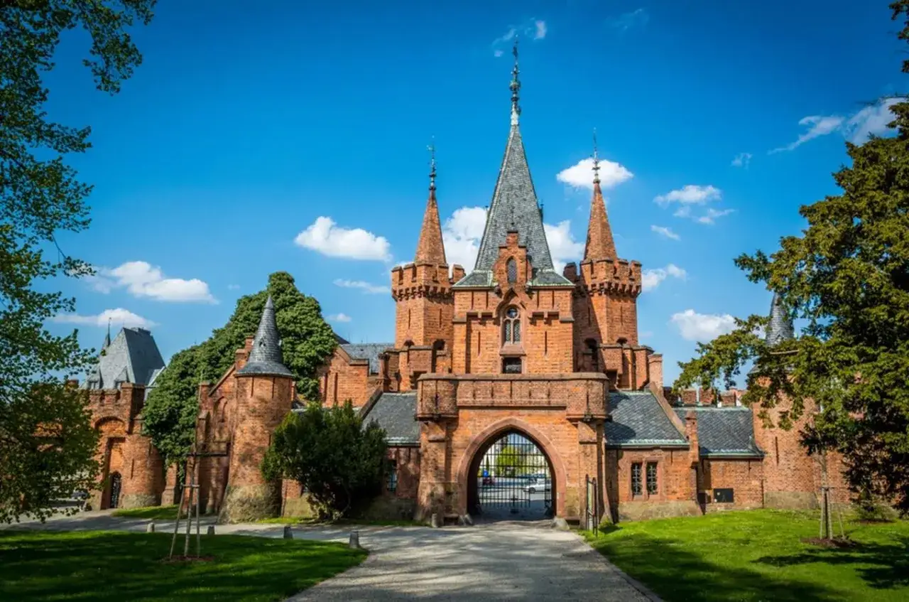 Imponujący zamek Hradec nad Moravicí z cegły, z licznymi wieżyczkami i bramą, pod błękitnym niebem.