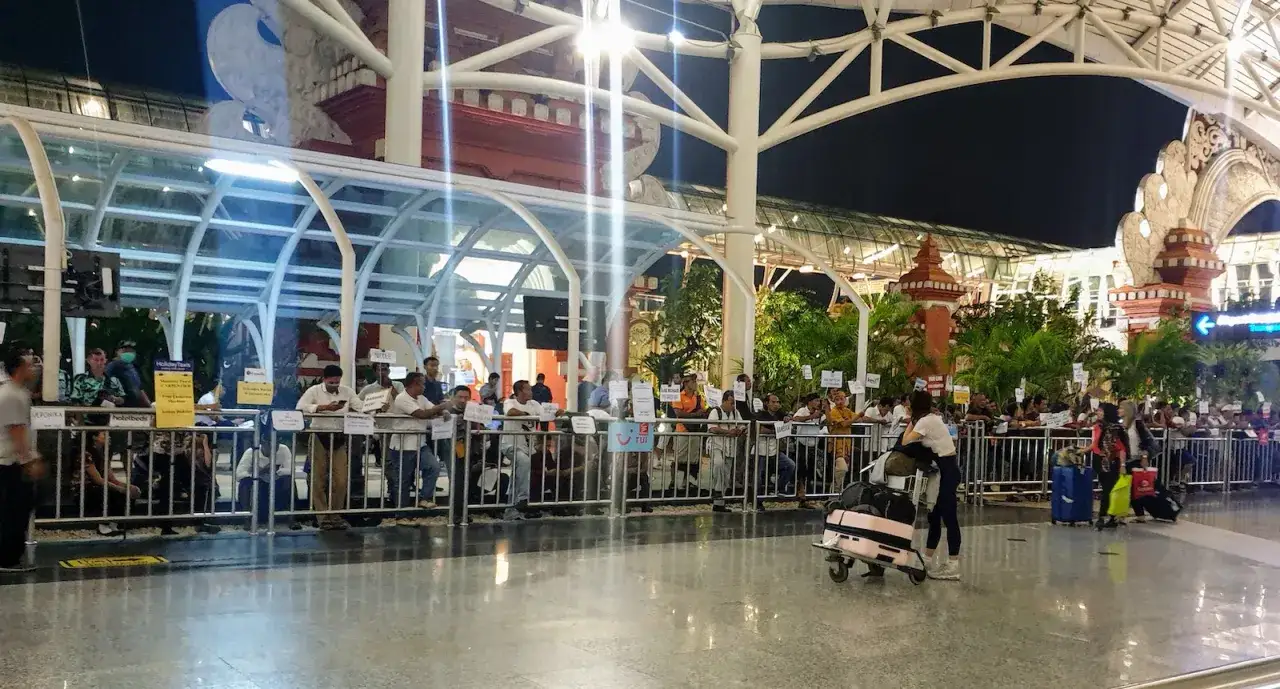 Ludzie czekają na odbiór na lotnisku w Denpasar na Bali. W tle widać charakterystyczną architekturę.