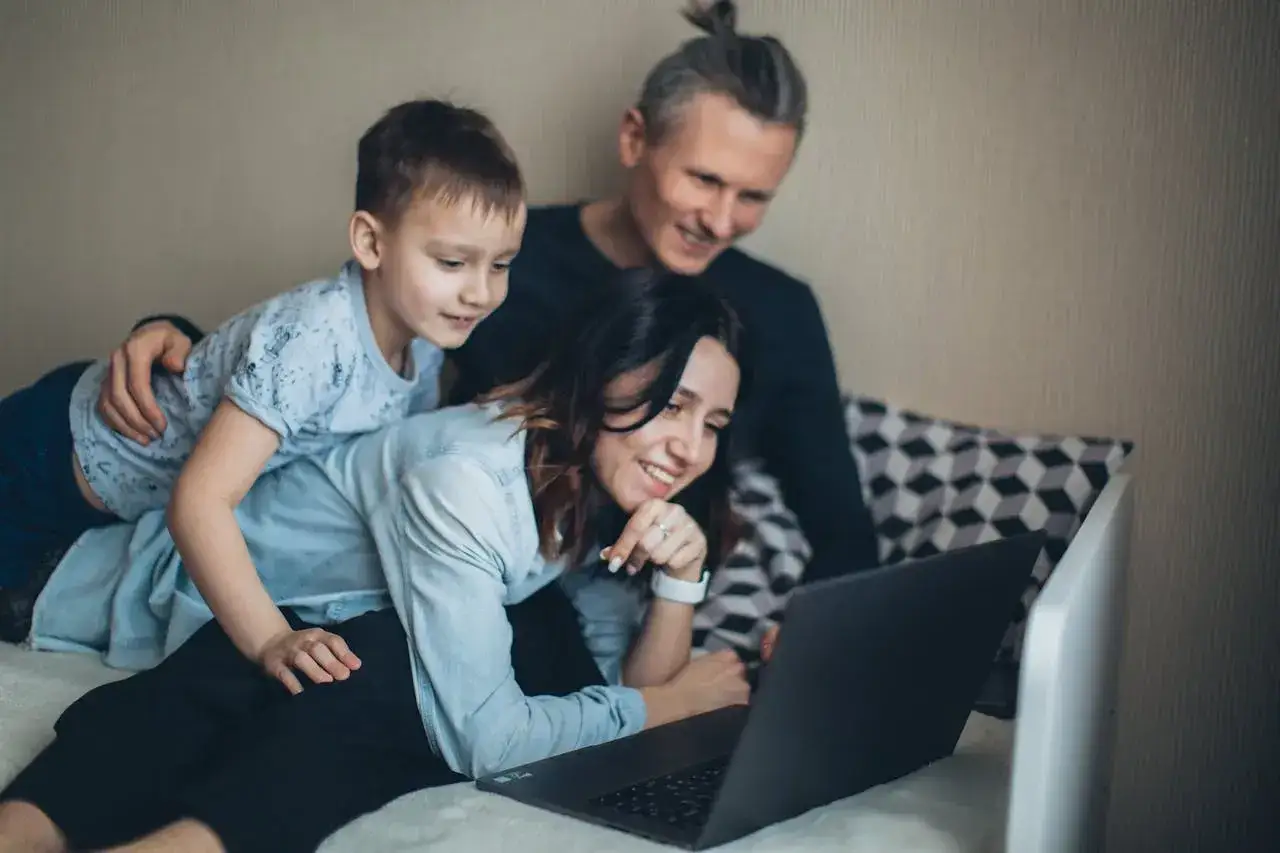 Rodzina ogląda coś na laptopie. Dziecko siedzi na mamie, a tata stoi za nimi. To jak darowizna od rodziców bez podatku, bo spędzają razem czas.