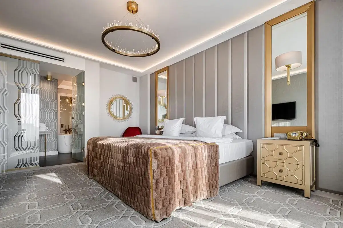 Elegancki pokój hotelowy, 4-gwiazdkowy, z luksusowym łóżkiem, kryształowym żyrandolem i złotymi dodatkami.