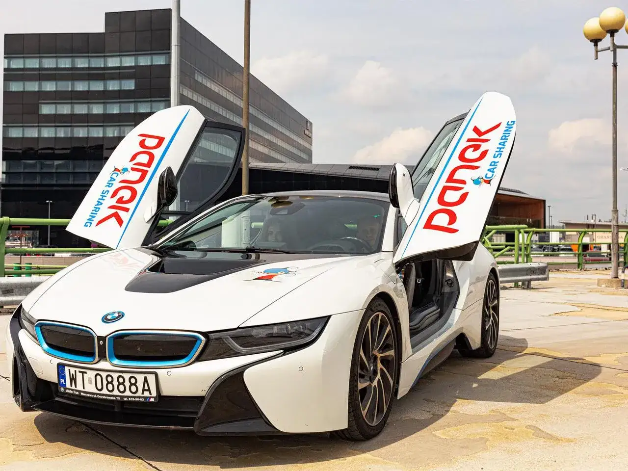 Białe BMW i8 z otwartymi drzwiami, na których widnieje logo Panek Car Sharing. Sprawdź panek cennik i wybierz się na przejażdżkę!