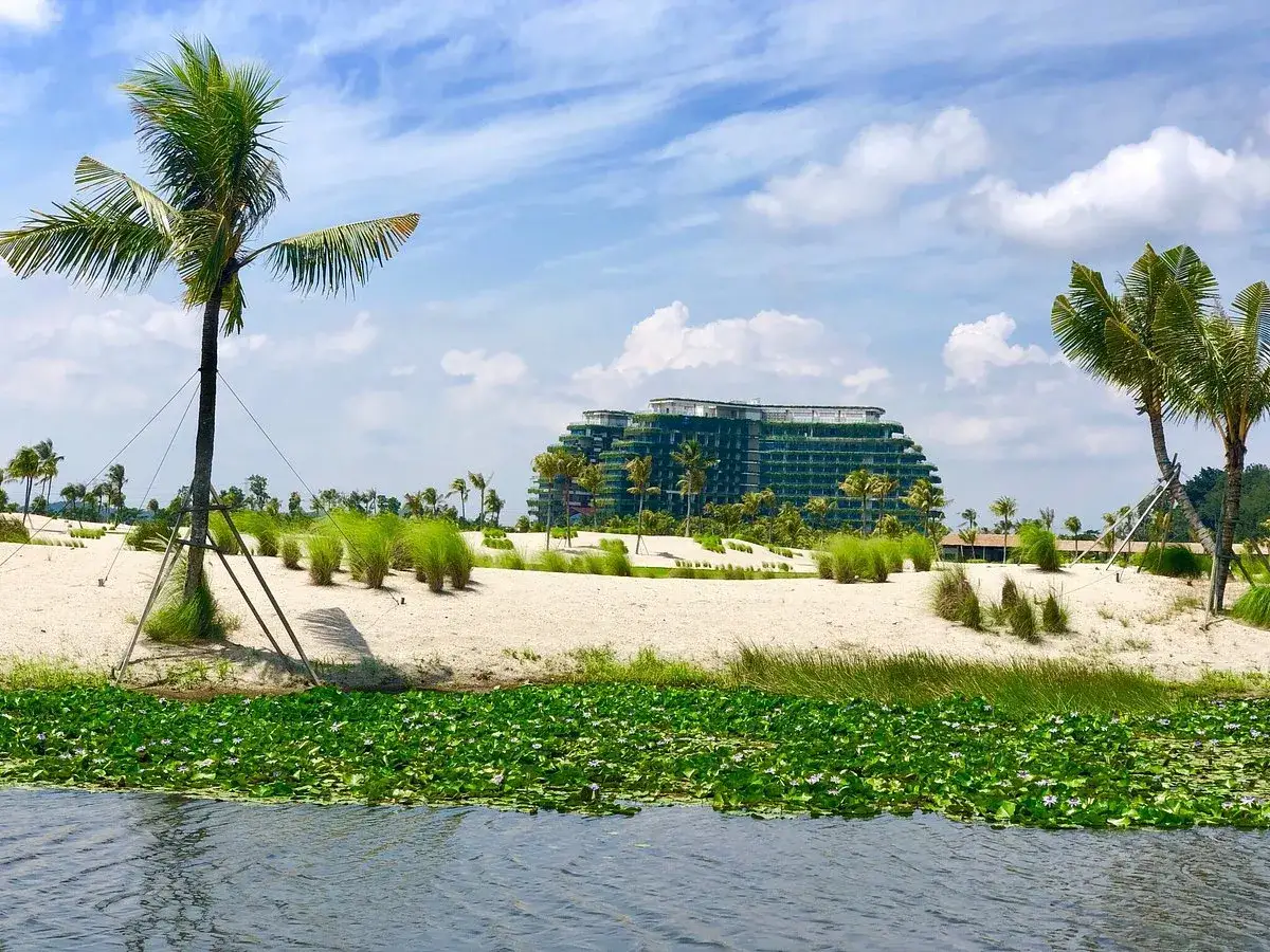 Tropikalny krajobraz z palmami i piaszczystą plażą, w tle nowoczesny hotel, który wygląda jak leśna miasto Malezja.