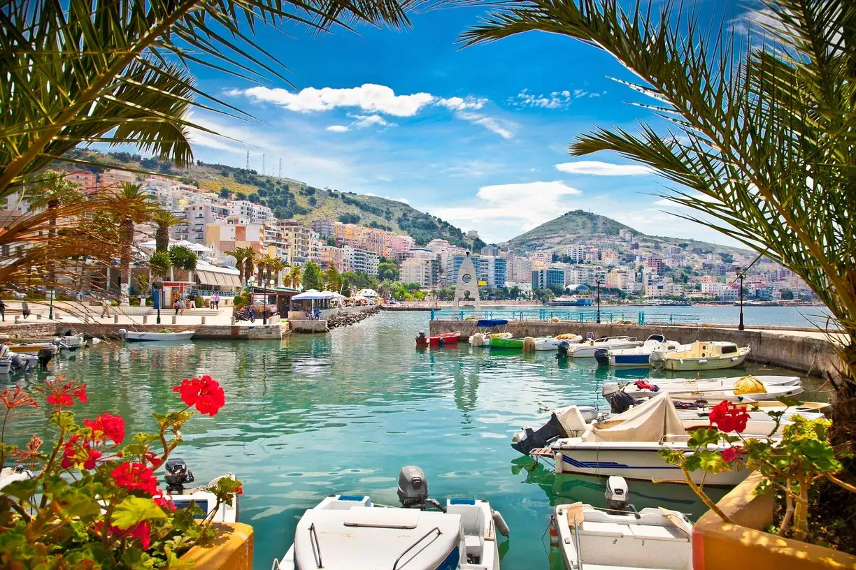 Malowniczy port z łodziami i palmami, idealne miejsce na albania wakacje. Miasto na wzgórzu, błękitne niebo i turkusowa woda.
