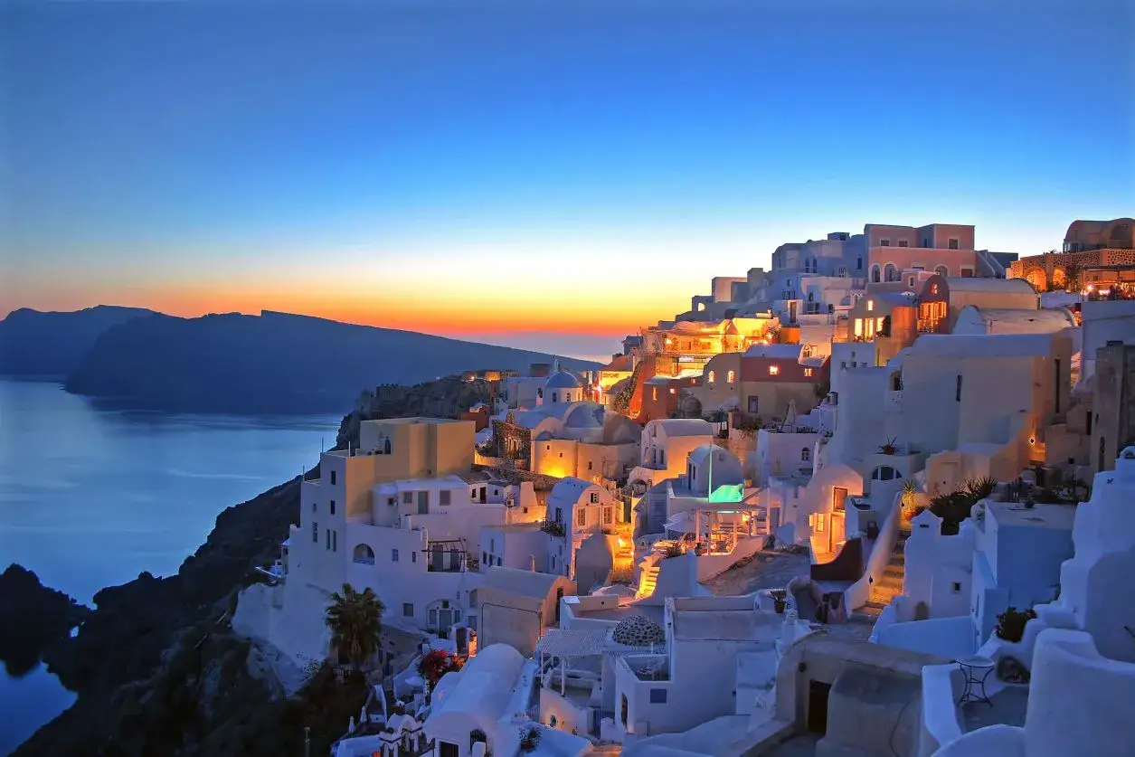 Santorini wakacje: białe domy na klifie o zachodzie słońca, morze i góry w tle. Idealne miejsce na wymarzone wakacje.
