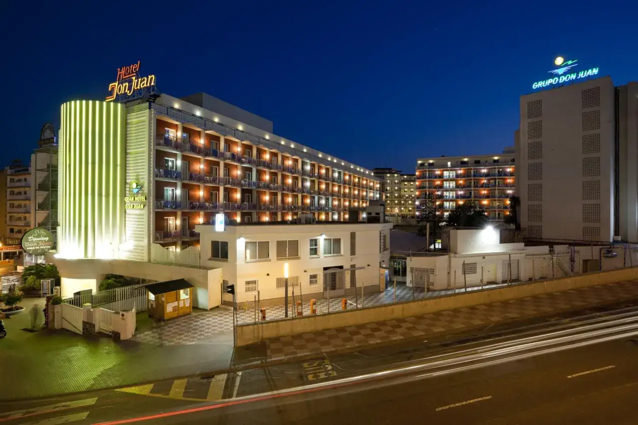 Hotel Don Juan Resort nocą, z neonowym oświetleniem i widocznymi światłami w oknach.