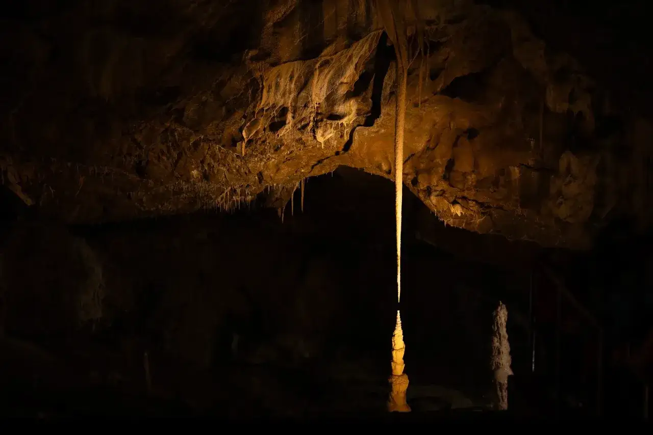 Wnętrze jaskini macochy, gdzie stalaktyt spotyka się ze stalagmitem, tworząc kolumnę. W tle widać inne formacje skalne i schody.