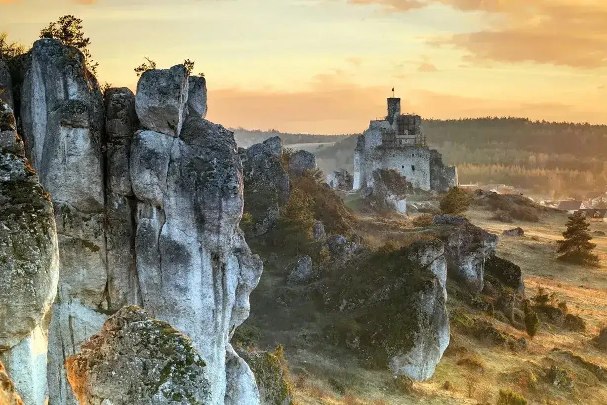 Skalny ostaniec góruje nad krajobrazem, na którym w oddali widać ruiny zamku.