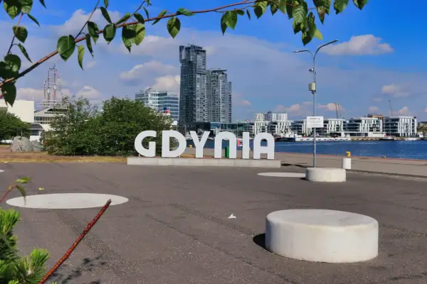 Napis "GDYNIA" na tle nowoczesnych budynków i portu.