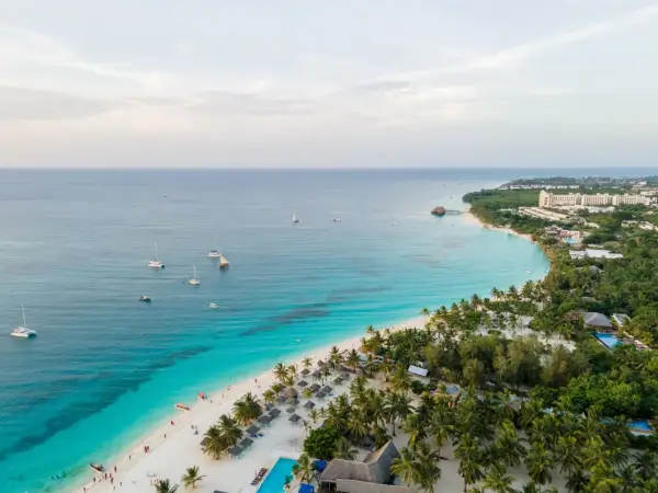 Rajska plaża na Zanzibarze z turkusową wodą, palmami i łodziami. Sprawdź aktualne zanzibar ceny, by zaplanować wymarzone wakacje.