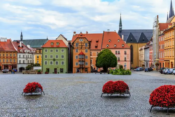 Kolorowy rynek w Chebie z kamienną nawierzchnią i ozdobnymi donicami z czerwonymi kwiatami.