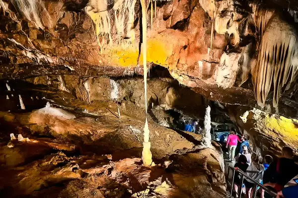 Wnętrze jaskini Macochy, z naciekami i stalagmitami. Grupa turystów schodzi po schodach, podziwiając podziemne piękno.