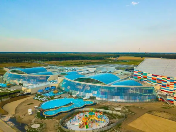 Nowoczesny, największy park wodny w Polsce z błękitnymi dachami i kolorową fasadą, otoczony zielenią.
