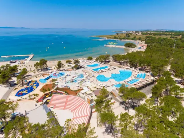 Widok z lotu ptaka na kompleks basenów i plażę z turystami w słoneczny dzień.