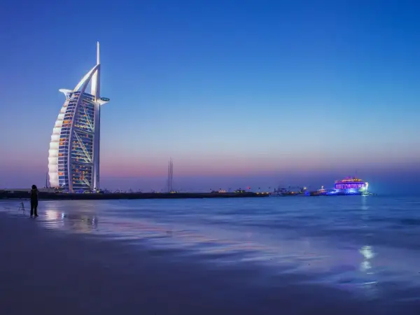 Wieżowiec Burdż al-Arab i oświetlony statek na tle nocnego nieba nad Zatoką Perską.